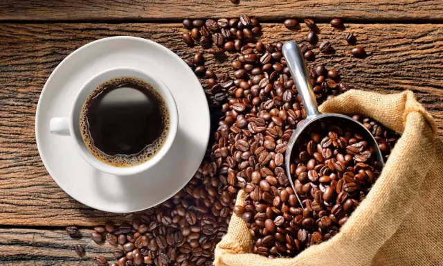 Eine Tasse heißer Kaffee neben einer Schaufel voller gerösteter Bohnen und einem Jutesack. Der Duft von perfekt gebrühtem Filterkaffee liegt in der Luft.