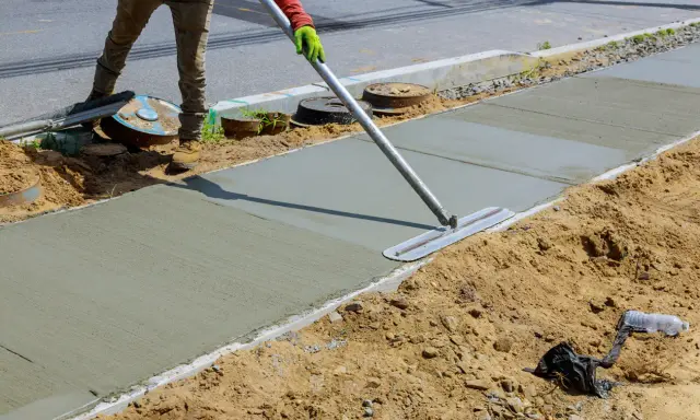 Robotnik wygładza świeży beton na chodniku za pomocą kielni.