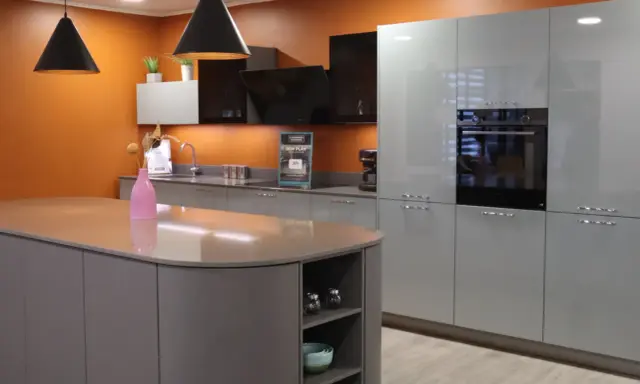 Cuisine moderne avec îlot central et armoires grises. Les murs orange vif contrastent avec les surfaces épurées, créant une ambiance chaleureuse. Une cuisine sans hotte, mais avec un design élégant.