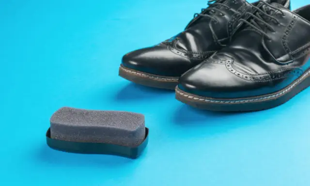 Czarne buty ze sztucznej skóry i gąbka do pastowania. Czy można pastować buty ze sztucznej skóry? Tak, specjalnymi preparatami.