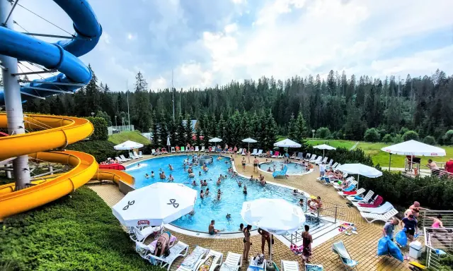 Aqua park Bukowina tętni życiem. Ludzie kąpią się w basenie, zjeżdżają ze zjeżdżalni i odpoczywają na leżakach.
