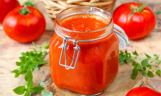 Un bocal de sauce tomate maison, avec des tomates fraîches et du basilic disposés autour.