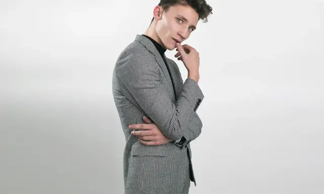 Elegancka stylizacja na 18 urodziny: młody mężczyzna w garniturze w drobną kratkę, czarny golf.