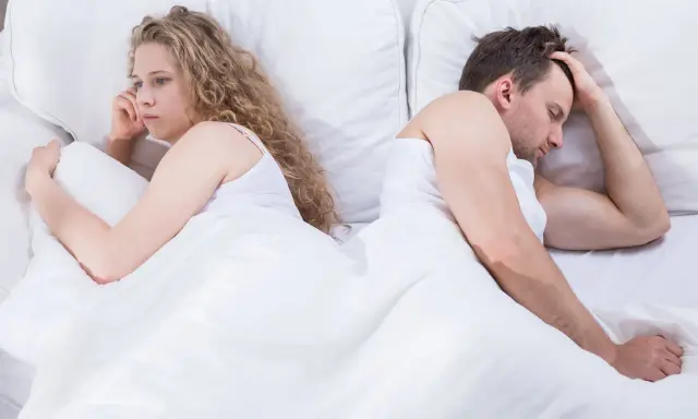 Para, odwróceni do siebie plecami w łóżku, zmartwiona kobieta i mężczyzna z ręką na czole. Czy to pochwica? Co to za problem?