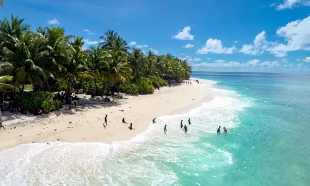 Spiaggia tropicale con palme e persone che nuotano nell'acqua cristallina dell'atollo di Maafushi.