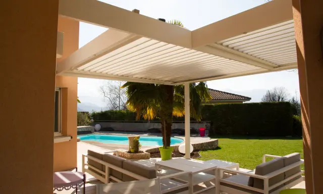Une pergola bioclimatique moderne avec des lames orientables protège un salon extérieur et une piscine.