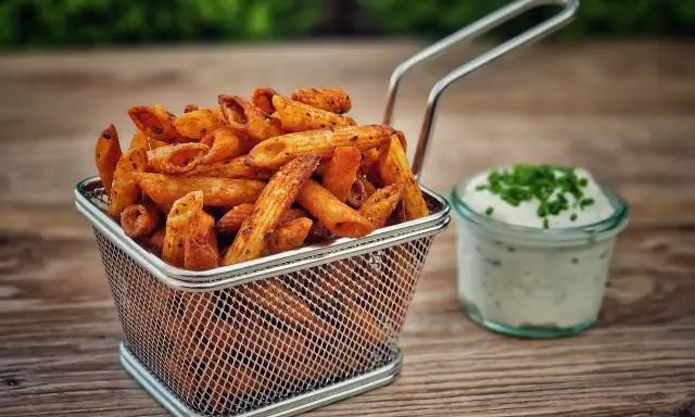 Knusprige Nudel-Chips in einem Metallkorb, daneben ein Glas Dip mit Schnittlauch.