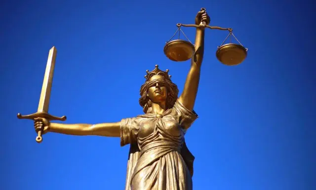 Statua dorata della Giustizia con spada e bilancia, simbolo dei giudici ordinari, contro un cielo blu intenso.