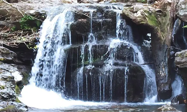 Cascada en el **valle de Cabuérniga**, con agua cayendo en varios niveles sobre rocas oscuras y musgosas, formando un remanso tranquilo.