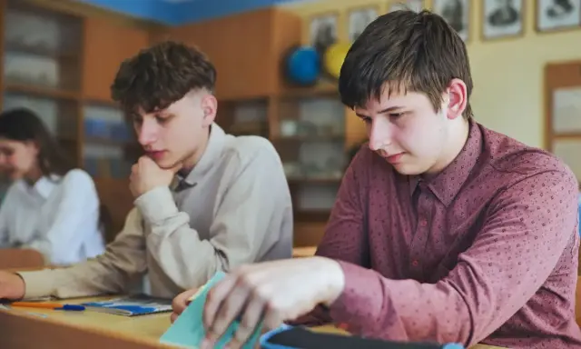 Uczniowie w klasie, jeden z nich zamyślony, inny przegląda notatki. Czyżby czekał na ocenę, która może oznaczać nieklasyfikowanie ucznia?