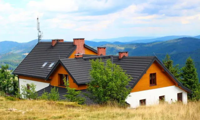 Wielka racza na dachu domu w górach, otoczona zielenią i widokiem na pasma górskie.