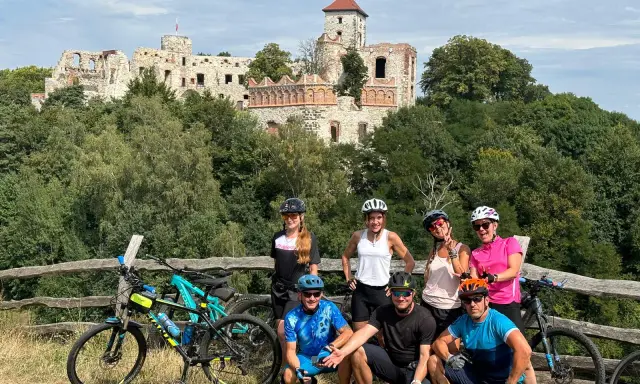 Grupa rowerzystów na tle ruin zamku. Planują noclegi na Szlaku Orlich Gniazd rowerem.