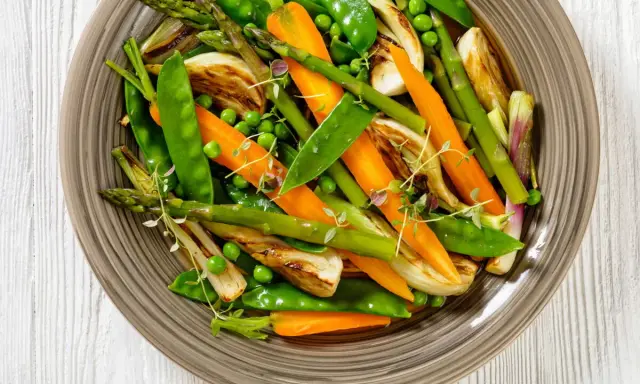 Jardinière de légumes colorée : carottes, pois, asperges et fenouil grillés, garnie de thym frais. Un plat sain et appétissant.