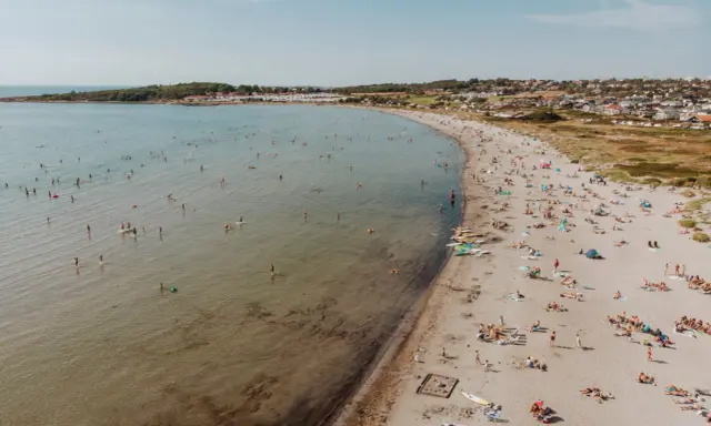 En livlig strand i Halland med många badande och solande människor. Vattnet är klart och inbjuder till lek.