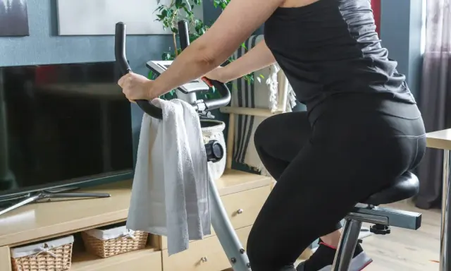 Kobieta w czarnym stroju ćwiczy na rowerze stacjonarnym, spędzając godzinę jazdy na rowerze stacjonarnym w domowym zaciszu.