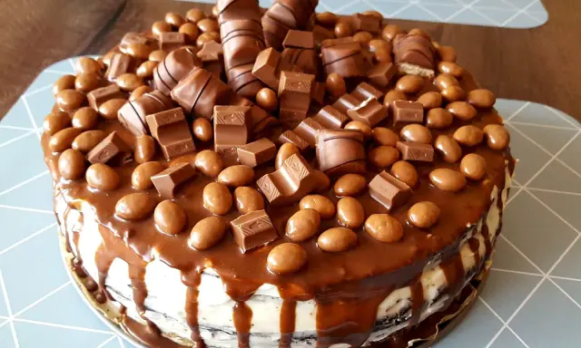 Pyszny tort kinder bueno, obficie udekorowany kawałkami batoników i czekoladowymi drażetkami, spływający karmelem.