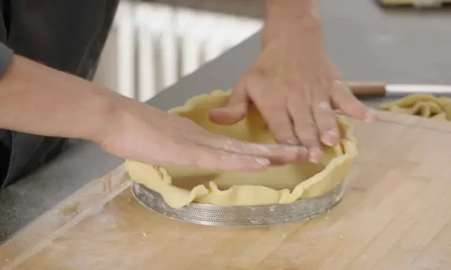 Mains expertes pour foncer une pâte dans un cercle à tarte. La pâte est étalée et ajustée sur les bords.