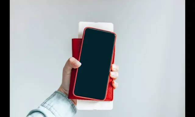 Dłoń trzyma iPhone'a w czerwonym etui. Czy iPhone jest bezpieczny? Zależy od użytkownika i jego nawyków.