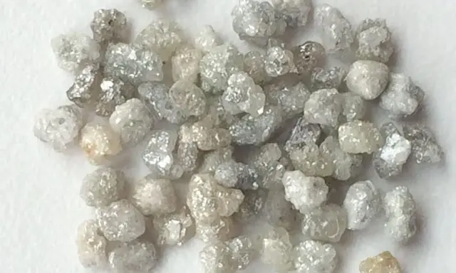 Un mucchio di grezzi diamanti non lavorati, con sfumature che vanno dal bianco al grigio e un leggero tocco dorato, pronti per essere trasformati.