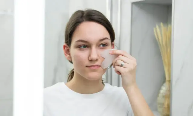 Une jeune femme utilise un gua sha pour un massage facial, un remède de grand-mère pour un visage gonflé.