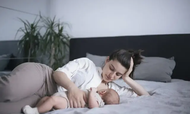 Mama karmi na leżąco swoje dziecko na łóżku. Czuły moment bliskości i spokoju.