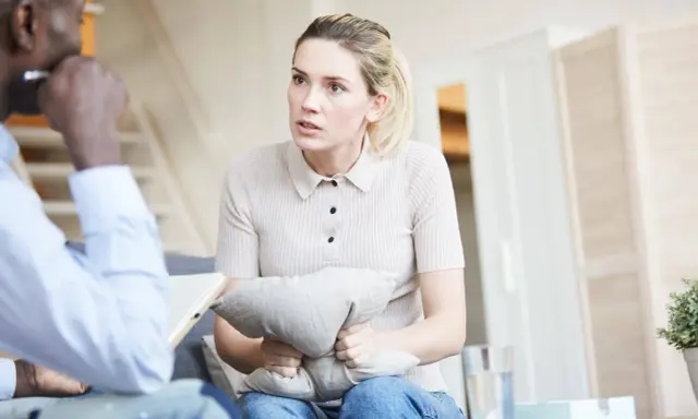 Kobieta trzyma poduszkę, rozmawiając z terapeutą. Czeka na zwolnienie od psychiatry, by móc wrócić do normalnego życia.