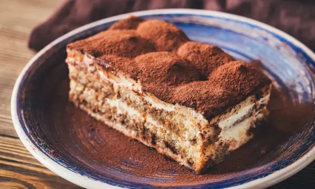 Pyszny kawałek tiramisu z mascarpone, posypany kakao, na talerzu. Idealny sprawdzony przepis na deser.