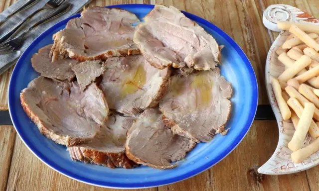 Plato azul con lonchas de jugosa carne mechada, servida con palitos de pan crujientes al lado.