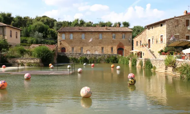 Paesini puglia con un laghetto pieno di sfere colorate, circondato da antichi edifici in pietra e vegetazione rigogliosa.