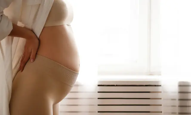 Donna incinta si tiene la schiena, forse per i crampi in gravidanza. Indossa una maglietta e una fascia di supporto.