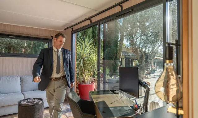 Un homme en costume entre dans un bureau lumineux avec vue sur un jardin. C'est la définition du home office : travailler depuis chez soi.