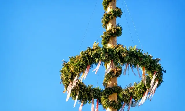 En midsommarstång, dekorerad med grönt och band, mot en klarblå himmel. Dess midsommarstång betydelse symboliserar sommarsolståndet och fruktbarhet.