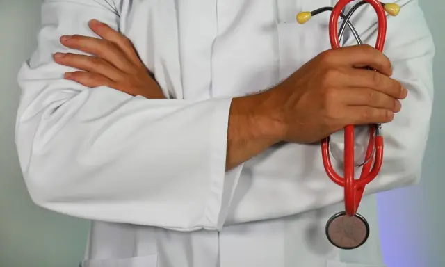 Lekarz w białym kitlu trzyma czerwony stetoskop. Dłonie skrzyżowane na piersi. Może to być pomocne przy diagnozowaniu zapalenia górnych dróg oddechowych.