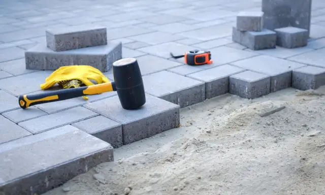 Beton pod kostkę czeka na ułożenie. Młotek gumowy, rękawice i miarka gotowe do pracy.