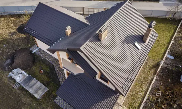 Nowy dach z ciemnej dachówki, z dwoma kominami i lukarną. Elewacja domu w odcieniach beżu i brązu. Facjata domu prezentuje się okazale.