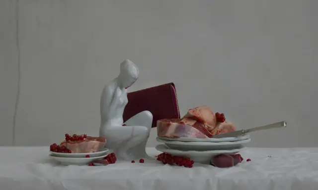 A white porcelain figure contemplates raw meat and red currants, a scene reminiscent of Evelyn Bencicova's still lifes.