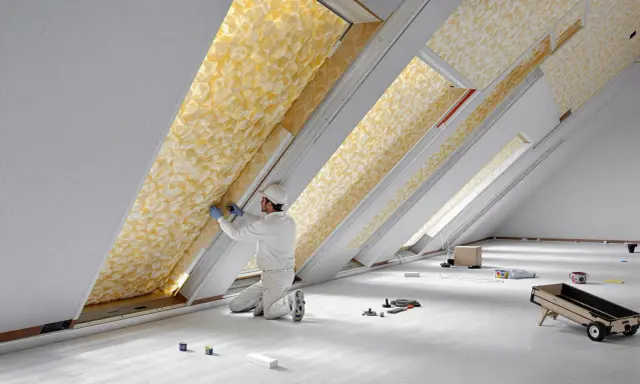 Un ouvrier installe un isolant thermique jaune texturé dans un grenier.