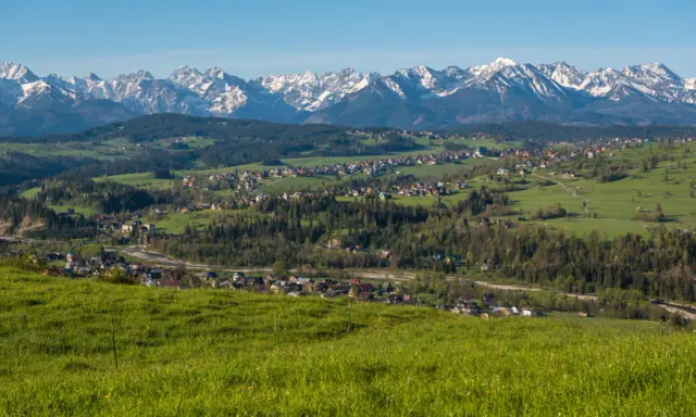 Widok na Tatry z zielonych wzgórz. W oddali widać zabudowania, które mogą być częścią trasy, ile km z Zakopanego do Bukowiny Tatrzańskiej.