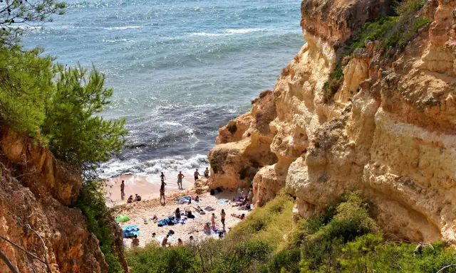 Sonnige Praia do Carvalho mit Felsen, grüner Vegetation und Badegästen am Meer.