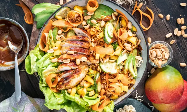 Ein bunter asiatischer Salat mit gegrilltem Hähnchen, Avocado, Mango, Karottenstreifen und Erdnüssen.