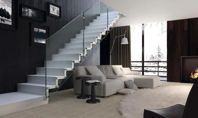 Escalera moderna de cristal con peldaños blancos y barandilla de vidrio en un salón luminoso.