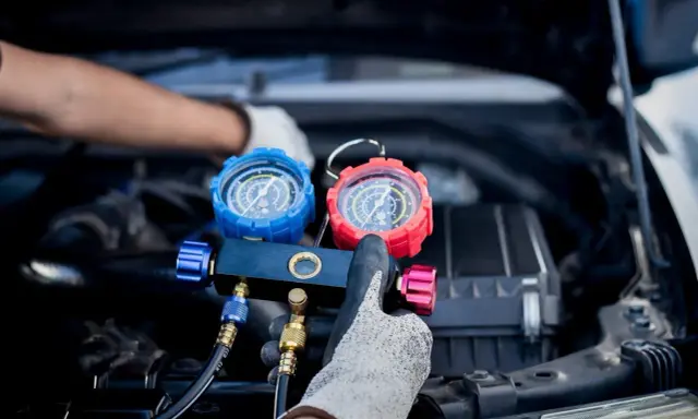 Manos enguantadas ajustan manómetros para saber como cargar aire acondicionado coche.