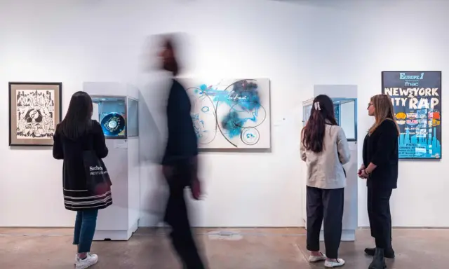 Visitors observe abstract art and a "New York City Rap" poster at a gallery exhibition.