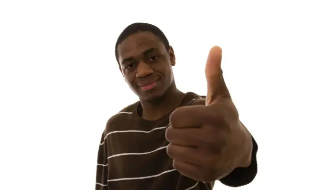 Un jeune homme souriant fait un pouce levé, un signe qui signifie "pas de soucis" ou "tout va bien".