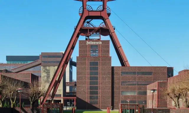 Industrielles Erbe mit rotem Förderturm und Backsteingebäuden. Die Zeche Zollverein strahlt eine starke, urbane Energie aus.