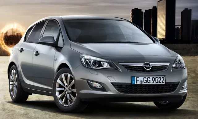 Szary Opel Astra 1.4 Turbo z nowoczesnymi światłami i felgami, na tle miejskiej panoramy i energetycznego kręgu.