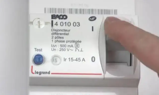 Main d'une personne actionnant le levier d'un disjoncteur différentiel Legrand, modèle 15-45 A.
