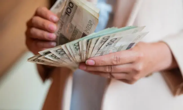Dłonie liczą banknoty 100 zł. To może być świadczenie pielęgnacyjne, które pomaga w codziennym życiu.