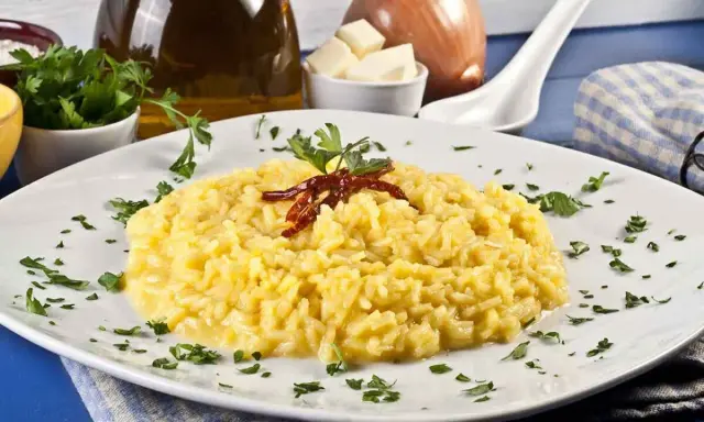 Aksamitne risotto alla milanese, ozdobione suszonymi papryczkami i natką pietruszki, prezentuje się apetycznie na białym talerzu.
