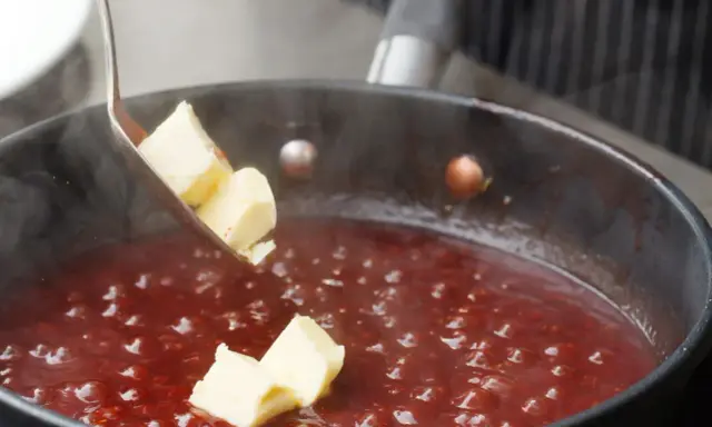 Butterstücke werden in eine köchelnde rote Sauce gegeben, um sie zu **saucen andicken** und zu verfeinern.